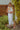 Woman in a white dress standing outdoors near greenery