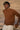 Man wearing a brown sweater and white pants standing next to a car with a blurred background