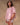 Woman wearing a pink, short-sleeved babydoll-style blouse and white bloomer shorts on a tan fabric background.