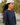 A woman outdoors wearing a navy blue quarter-sleeve top with yellow contrast stitching and a white beanie, captured in a side-profile portrait with wind-blown hair.