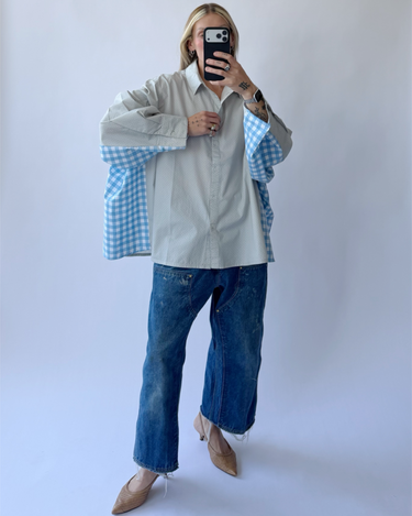 Person wearing a light gray shirt over a blue checkered shirt with blue jeans against a white background