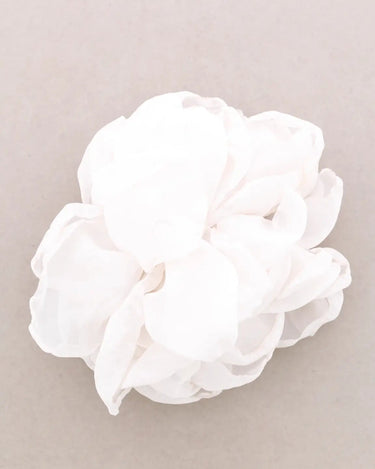 A white ruffled fabric flower accessory, likely a hair clip or decorative flower, shown on a neutral light gray background.