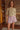 Woman wearing a green knit cardigan and pink plaid boxer-style shorts in a room with wooden walls and shelves.