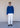 Man wearing a blue sweater with white jeans against, paired with brown boots.