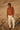 Person wearing a brown sweater and white pants standing in a dry, open field.
