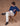 Man wearing a blue sweater with white jeans against a brown background.
