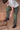 A man wearing a white t-shirt and green pants against a brown background.