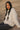 Woman wearing a white cable knit sweater sitting on sand dunes.