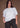 Woman wearing a white t-shirt and black pants against a brown background.