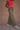 Woman wearing a red smocked top and army green military-style pants on a tan background.
