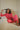 Woman sitting on a couch indoors and wearing a red blouse and pants set.
