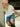 Woman in white blouse and denim shorts leaning against a wall with a blurred background