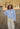Woman standing in a field outdoors wearing a light blue wool jacket and cream pants.