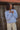 Woman standing outdoors wearing a light blue wool jacket and cream pants.