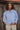 Woman standing outdoors wearing a light blue wool jacket and cream pants.