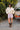 Woman in a cream cable knit sweater and pink plaid boxer-style shorts standing outdoors next to a vintage Volvo car.