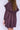 Close-up of a woman wearing a purple knee-length dress with long sleeves and a ruffled collar on a white fabric backdrop.
