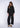 Woman wearing a black, rolled hem sweater and matching black sweater pants on a white fabric background.