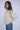 Woman wearing a cream knit sweater and blue jeans against a white background.