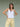 Woman wearing a white tank top and yellow pants on a plain background.