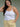 Woman wearing a white tank top and yellow pants on a plain background.
