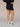 Woman wearing black knit shorts and white sneakers on a tan fabric backdrop.