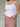 Woman wearing a white tank top and a pink gingham skirt on a plain background.