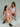 Two women wearing white tank tops and shorts on a plain background. One woman is squatted down and the other woman is sitting.