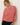 A woman wearing a red and white striped long-sleeve top and dark blue jeans, standing against a plain off-white wall.