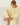 A woman sits cross-legged on a white wooden floor wearing a pale yellow lounge set consisting of a long-sleeve sweater and matching pants.