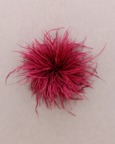 A bright magenta-pink fluffy feather accessory, centered on a plain light beige background.
