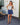 A woman modeling a tan strapless tube top and navy blue shorts, standing outdoors against a white brick wall.