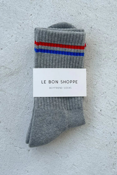 Gray socks with red and blue stripes on a textured white surface, featuring 'Le Bon Shoppe' label.