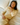 Woman wearing a yellow knit sweater with matching knit shorts on a bed with a floral patterned pillow and sheets.