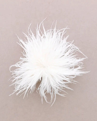A fluffy white feather pom-pom accessory photographed from above on a plain warm taupe background.