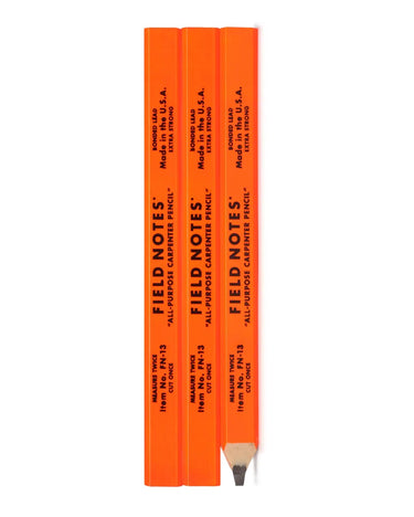 Three bright orange carpenter pencils stacked horizontally, with the top pencil uncapped and resting in front to show the wood grain and tip. The pencils are branded with 'FIELD NOTES' in black text.