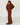 A woman wearing a matching dark red long-sleeve top and wide-leg pants set, standing in a minimalist white room with light wood floors.