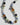 A beaded necklace with a mix of polished black, metallic silver, light green, pale blue, translucent amber, and frosted white beads, arranged in a U-shape on a light gray background.