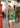 Woman in a green cardigan and white shorts using a phone on a city street.