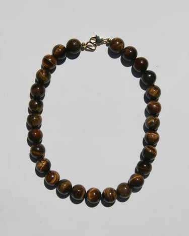A beaded necklace made of polished brown tiger's eye beads with a small gold clasp, displayed on a plain light gray background.