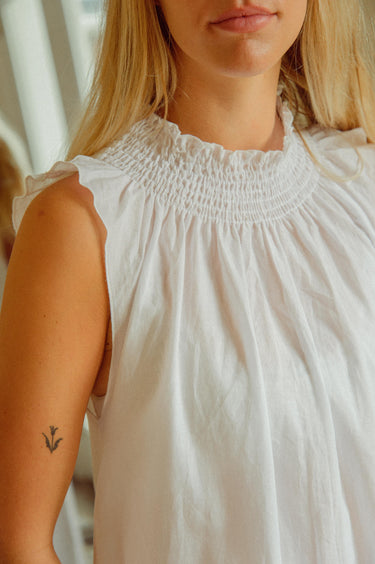 Woman wearing a white sleeveless top with a blurred background