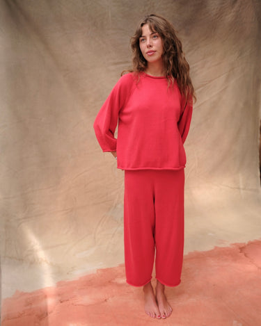 Woman wearing a red, rolled hem sweater and matching red sweater pants on a tan fabric background.