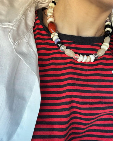 Person wearing a red and black striped shirt with a beaded necklace.