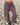 A person wearing loose, wide-leg pleated trousers in a small-scale checkered pattern of blue and red, standing on a bed of light gray pebbles.