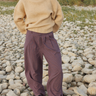 A person standing on a rocky outdoor shoreline wearing a cream knit mock-neck sweater and loose blue plaid pleated trousers with black shoes.