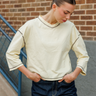 A woman wearing a yellow quarter-sleeve top with navy blue piping details on the neckline and cuffs, paired with dark blue jeans, standing in front of a brick wall.