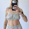 Person wearing a light gray sleeveless top and pants, taking a mirror selfie.