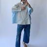 Person wearing a light gray shirt over a blue checkered shirt with blue jeans against a white background