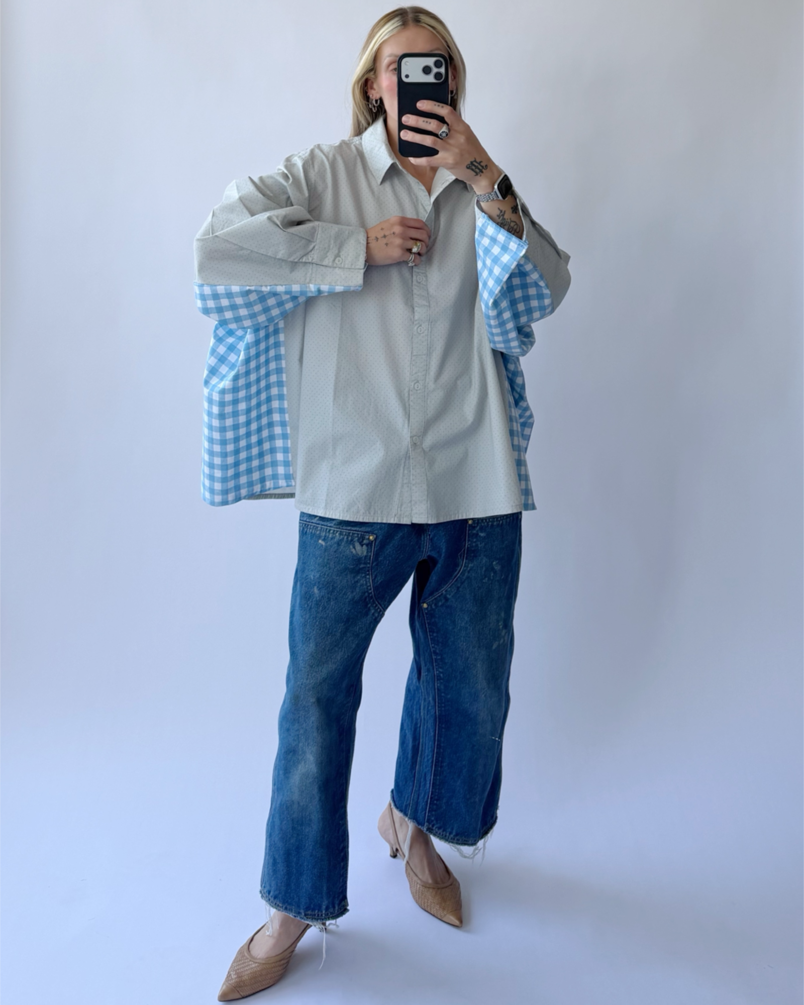 Person wearing a light gray shirt over a blue checkered shirt with blue jeans against a white background