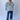 Person wearing a light gray shirt over a blue checkered shirt with blue jeans against a white background